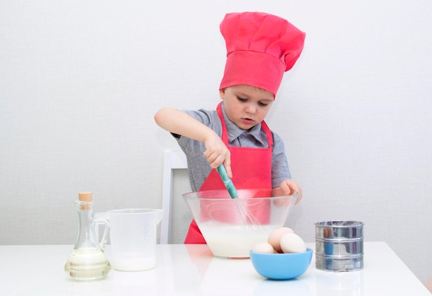 Cute little boy in a red chef hat kneads the pastry dough in a bowl. Homemade cakes.