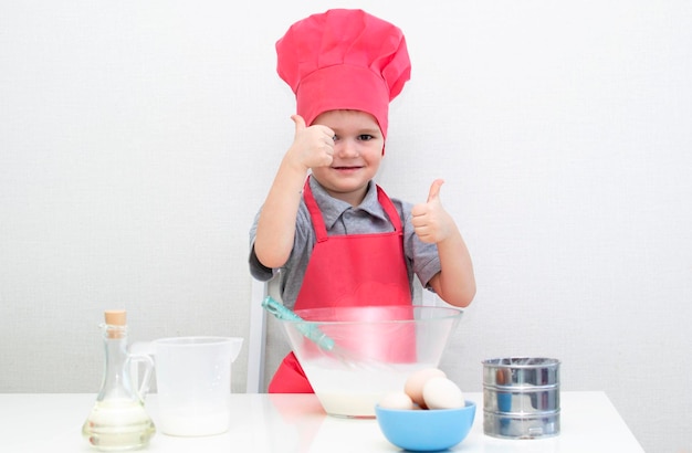 Cute little boy in a red chef hat kneads the pastry dough in a bowl. Homemade cakes.