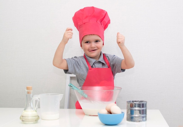 Cute little boy in a red chef hat kneads the pastry dough in a bowl. Homemade cakes.