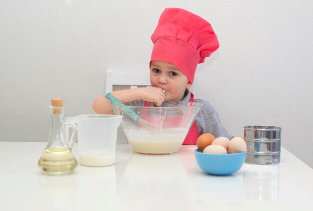 Cute little boy in a red chef hat kneads the pastry dough in a bowl. Homemade cakes.