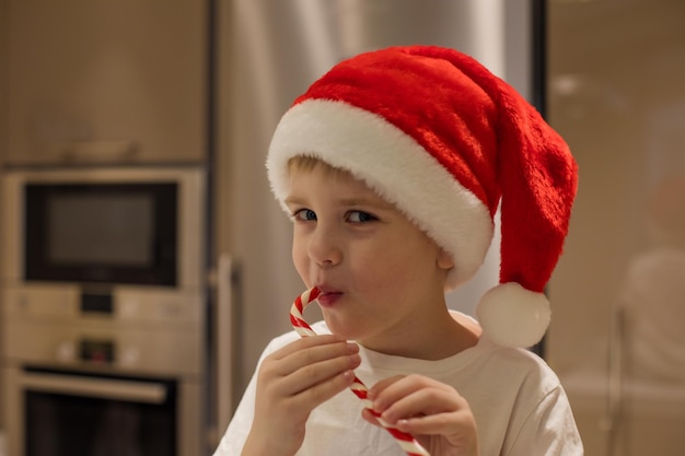 A cute little boy in Santa Claus Christmas red cap eats a striped lollipop Concept holiday sweets