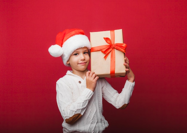 Cute little boy in a Santa Claus hat holding a gift box on a red background a child with a New Year's gift for Christmas new year