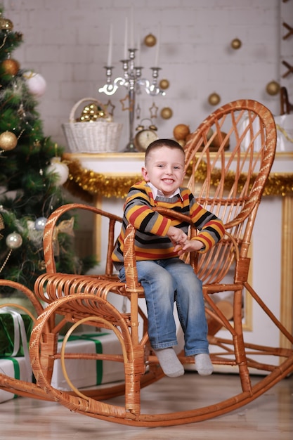 Cute little boy sitting in rocking chair near christmas tree.