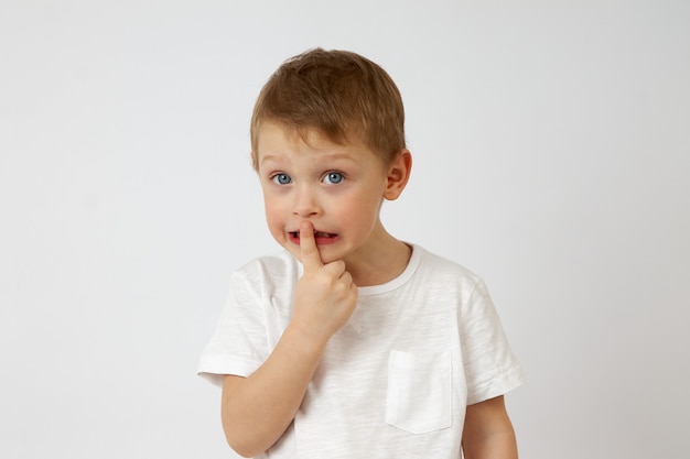 Cute little boy standing on a white background and putting his index finger to his lips