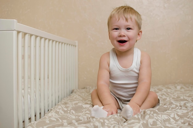 Cute little boy toddler sits on a bed in the bedroom and surprised smiles