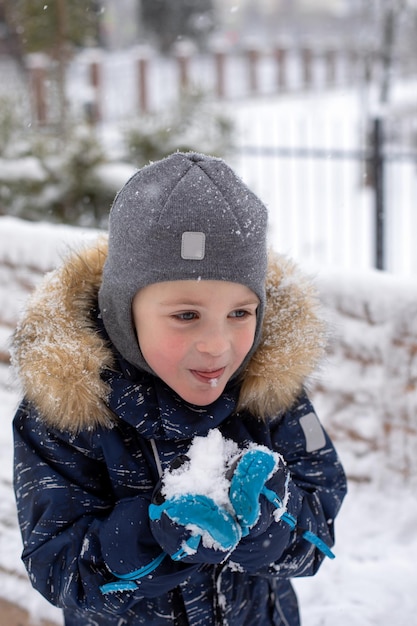 Cute little boy tries to eat snow with his tongue in the winter on the street He is having fun