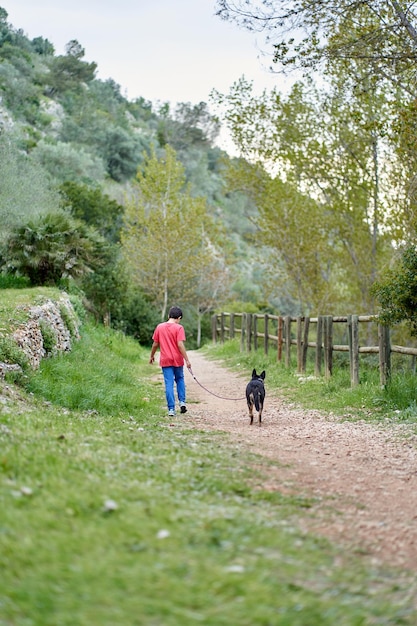 Cute little boy, walking his little pet dog in rural rapeseed field next to him, boy walking on a small path