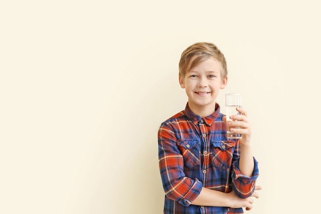 Cute little boy with glass of water on color