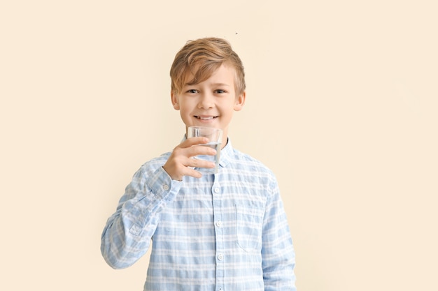 Cute little boy with glass of water on color