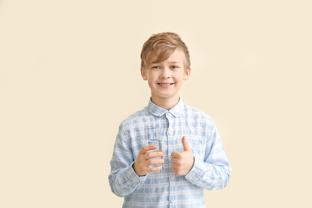 Cute little boy with glass of water showing thumb-up on color