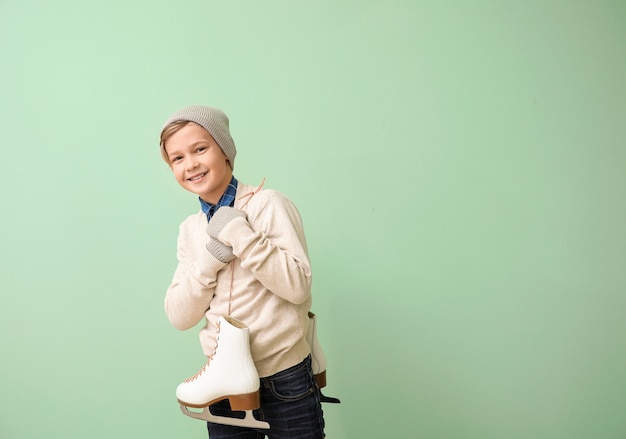 Cute little boy with ice skates against color