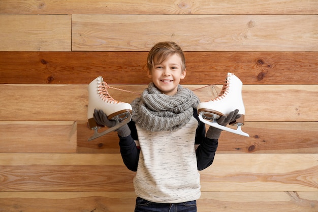 Cute little boy with ice skates against wooden