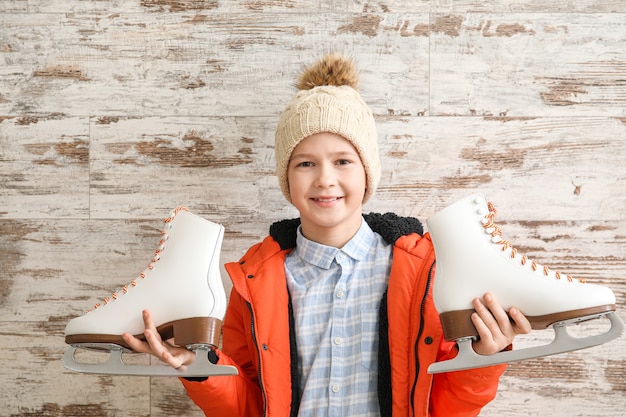 Cute little boy with ice skates against wooden