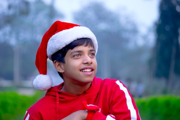  A cute little boy with Santa cap red t-shirt, smiling happily and looking away at a distance 