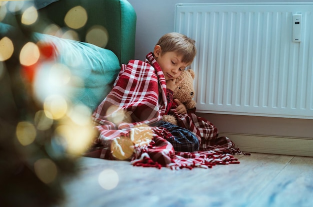 Cute little boy wrapped id plaid sitting by heater