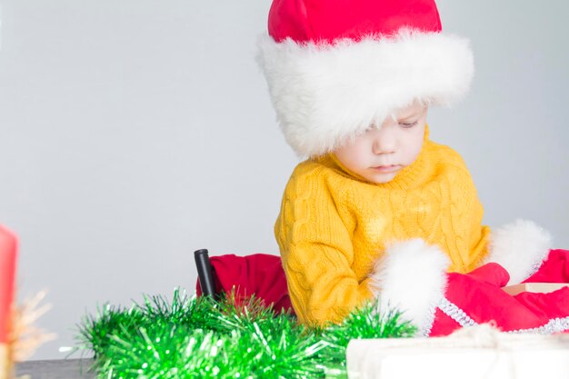 A cute little boy in a yellow sweater a red Santa Claus hat and Christmas mittens with gifts in his hands