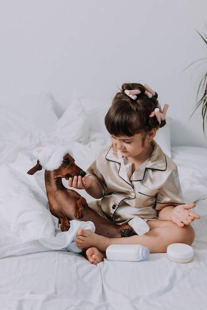 cute little brunette girl at home in bed with a dog playing with baby cosmetics. little lady