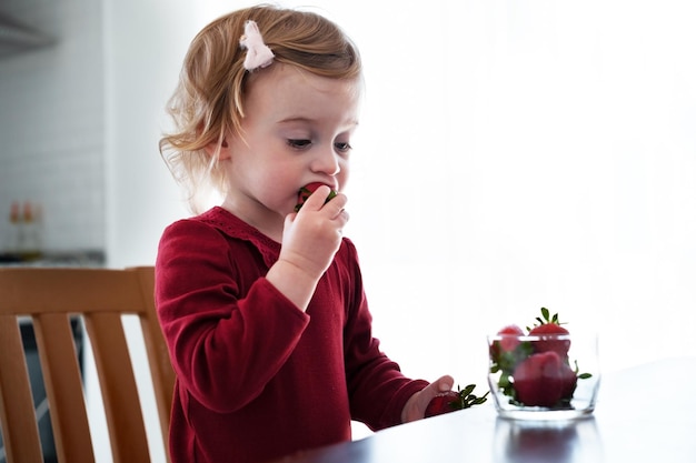 Cute little caucasian blonde baby girltoddler prettyadorable infant eating strawberry from table in