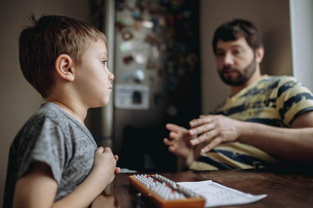 Cute little caucasian boy doing his mental arithmetic homework with father sitting next to him at the kitchen table. High quality photo