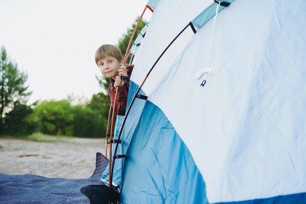 Cute little caucasian boy looking out from touristic tent Family camping concept