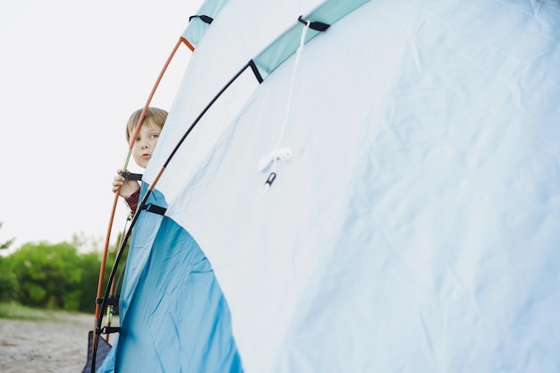 Cute little caucasian boy looking out from touristic tent Family camping concept