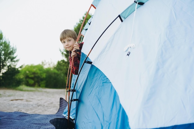 Cute little caucasian boy looking out from touristic tent Family camping concept