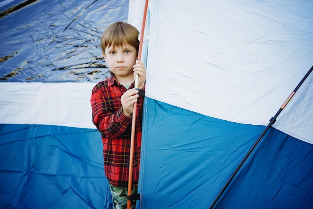 Cute little caucasian boy looking out from touristic tent Family camping concept