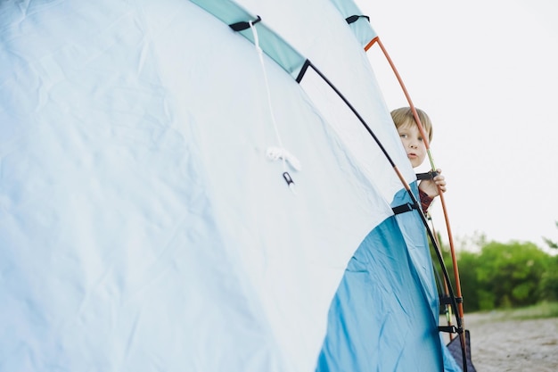 Cute little caucasian boy looking out from touristic tent Family camping concept