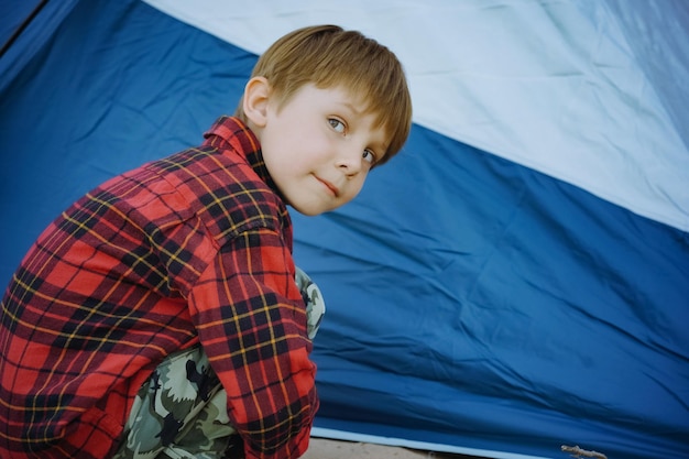 Cute little caucasian boy sitting on sand barefoot by touristic tent Family camping concept