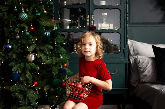 Cute little child girl playing with Christmas decoration near Christmas tree indoors Merry Christmas and Happy Holidays