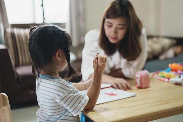 Cute little child painting with colorful paints Asian girl and mother using crayon drawing color Daughter and mom doing homework coloring cartoon characters Baby artist activity lifestyle concept