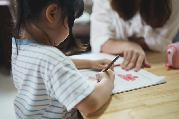 Cute little child painting with colorful paints Asian girl and mother using crayon drawing color Daughter and mom doing homework coloring cartoon characters Baby artist activity lifestyle concept