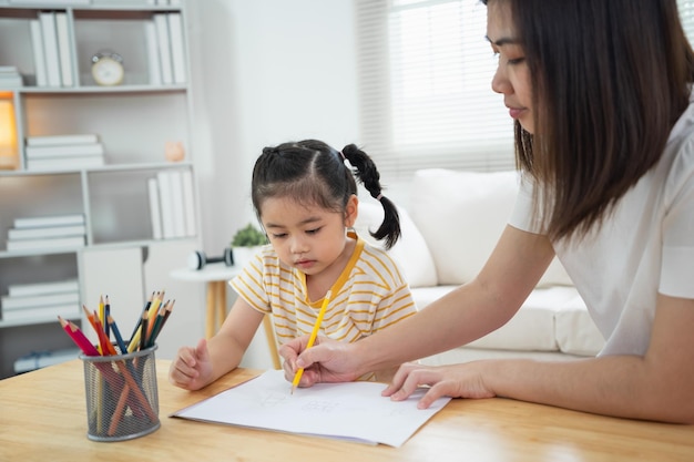 Cute little child painting with colorful paints Asian girl and mother using crayon drawing color Daughter and mom doing homework coloring cartoon characters Baby artist activity lifestyle concept