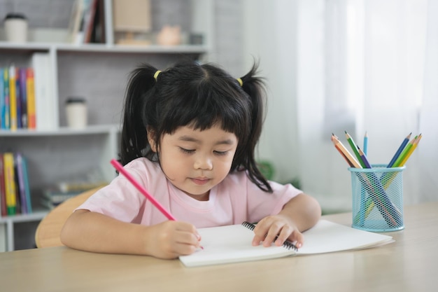 Cute little child wearing pink shirt holding pencil or doing homework or wood color painting with colorful paints Asian girl using wood color drawing colorBaby artist activity lifestyle concept