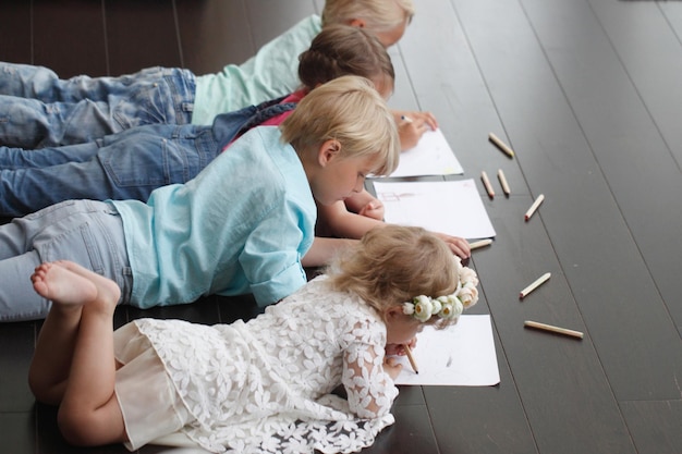 Cute little children friends drawing with pencils at home laying on floor