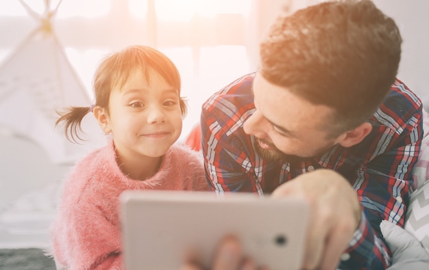 Cute little daughter and her handsome young dad are playing together in child's room. Daddy and child spend time together while sitting on the floor in bedroom.