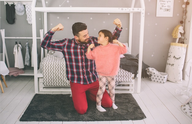 Cute little daughter and her handsome young dad are playing together in child's room. Daddy and child spend time together while sitting on the floor in bedroom.