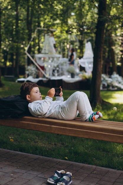 Cute little european child focused on smartphone in a bench at the park