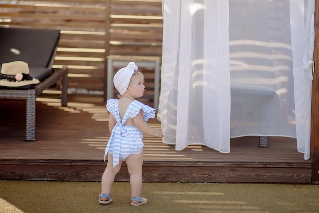 Cute little girl 1 year old on the beach at the resort in summer in a trendy outfit