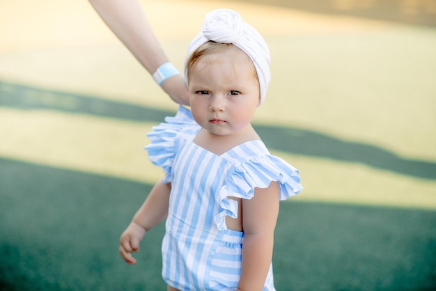 Cute little girl 1 year old on the beach at the resort in summer in a trendy outfit