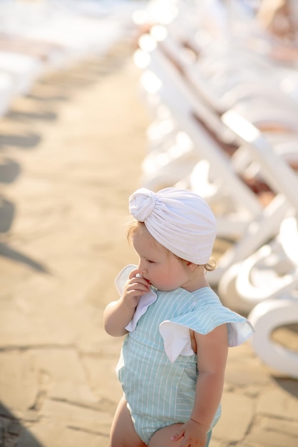 Cute little girl 1 year old on the beach at the resort in summer in a trendy outfit