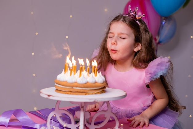 Cute little girl in a beautiful dress makes a wish and blows out the candles on the birthday cake