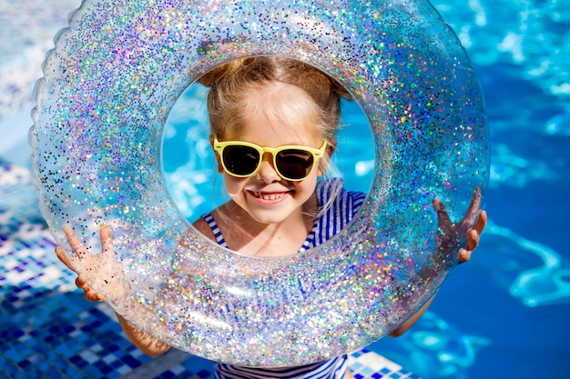 Cute little girl blonde in sunglasses laughs in the pool holding a lifeline