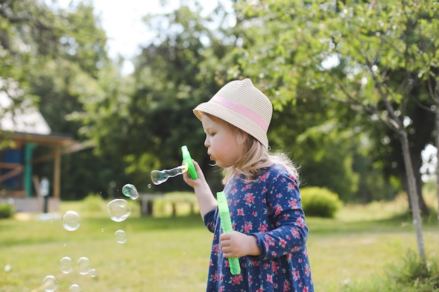 Cute little girl blowing soap bubbles on a walk in summer outdoors