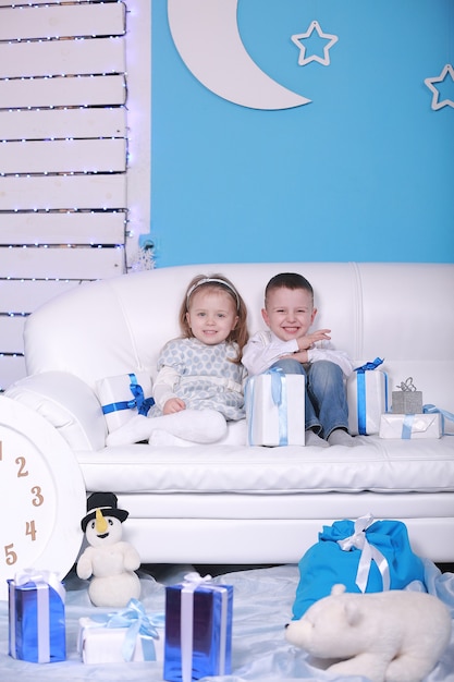 Cute little girl and boy with gift boxes sitting on a white sofa. celebrating Christmas and New Year.