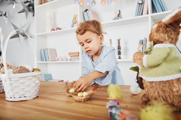 Cute little girl celebrating Easter holidays indoors near table with eggs