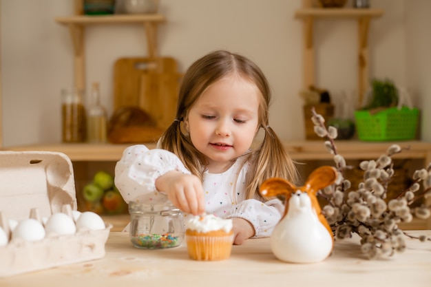 Cute little girl in a cotton dress at home in a wooden kitchen prepares an Easter cake