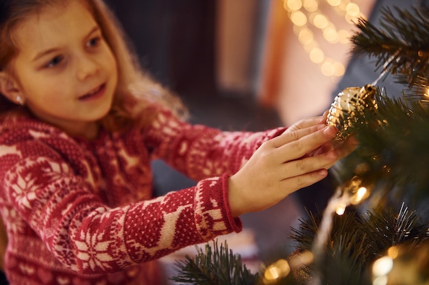 Cute little girl decorating christmas tree indoors at new year holidays.