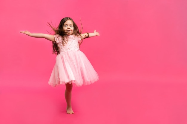 Cute little girl dreams of becoming a ballerina. Little Dancing Girl. Studio Shoot Over Pink Background.