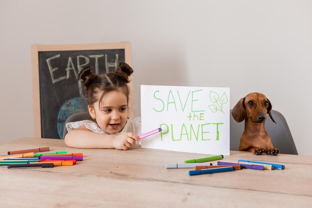 A cute little girl drew a sign quotsave the planetquot with her pet dog dachshund